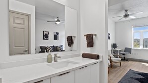 A modern bathroom with a large mirror, white countertops, a sink, and a ceiling fan.
