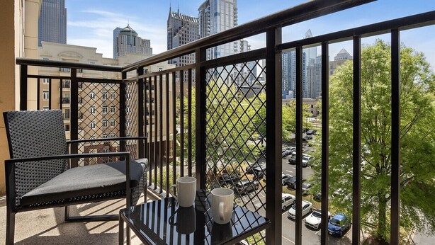 A balcony with a view of city buildings, a chair, and two mugs on a table.