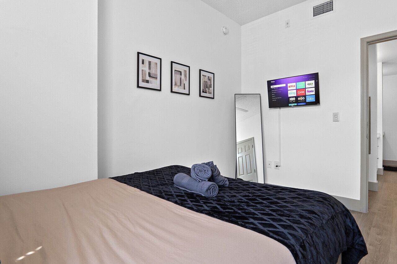 Ein Hotelzimmer mit einem Bett, einem flachbildfernseher an der Wand und einer Tür zu einem anderen Raum.