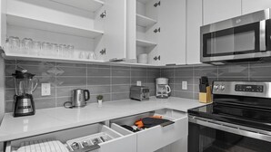 A modern kitchen with white cabinets, a microwave, a coffee maker, and a toaster. - Midnight Marvel | Amazing City Views, Free Parking (Charlotte)