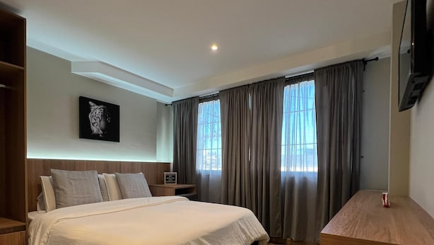 A modern bedroom with a large bed, wooden flooring, a mounted TV, and a window with curtains. - Aerosuites (Bogotá)
