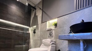 A modern bathroom with a glass shower enclosure, a white toilet, a black sink, and a towel rack. - Aerosuites (Bogotá)