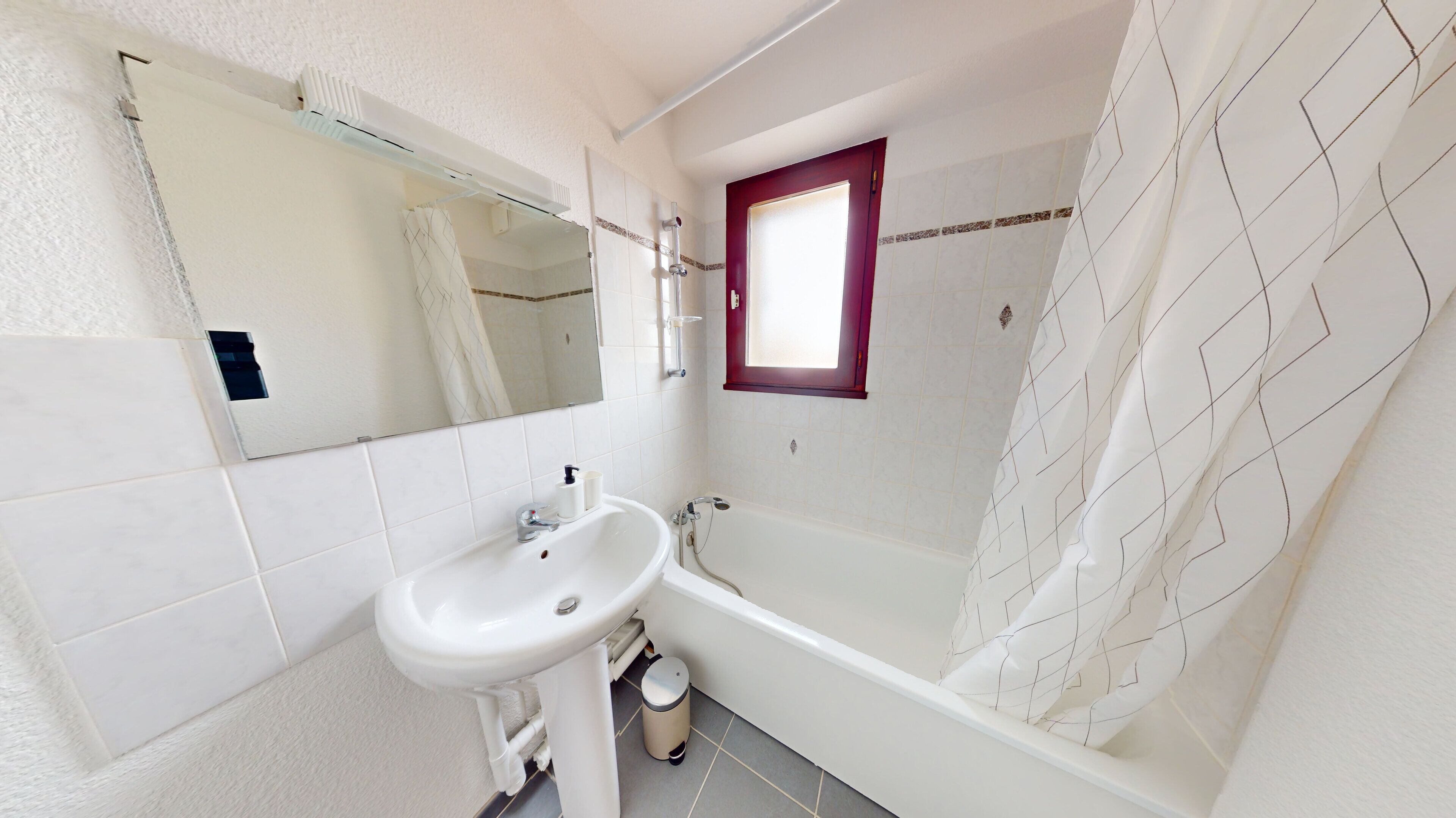 A bathroom with a white sink, a mirror, a window, and a shower area.
