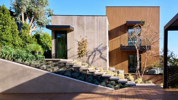 Una casa moderna con una terrazza in legno, una scala in cemento e una piscina.