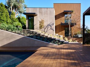 Une maison moderne dotée d’une terrasse en bois, d’un escalier en béton et d’une piscine.