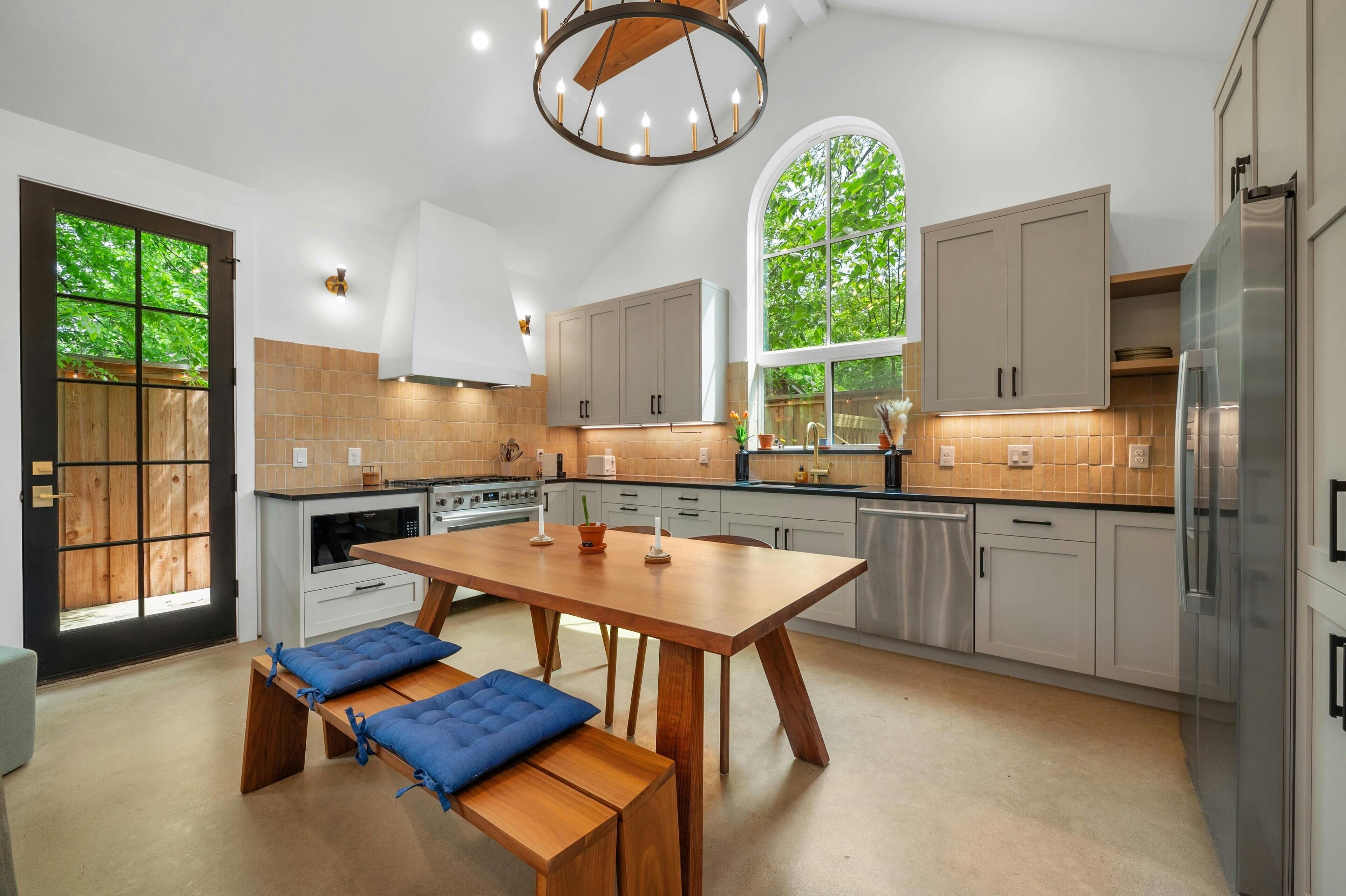 A modern kitchen with a large island, built-in appliances, and a large window.