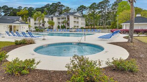 Un espace piscine avec des chaises longues, un jacuzzi et un bâtiment doté de balcons.
