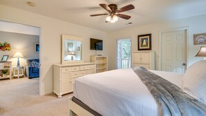 Une chambre à coucher comprenant un lit, un ventilateur de plafond, une commode, un téléviseur et une porte donnant sur un balcon.