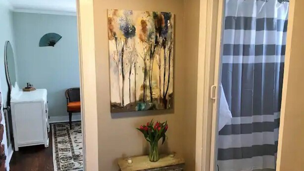 A hallway with a painting of trees, a small table with a vase of flowers, and a checkered shower curtain. - The Alexandria House #3
 (Jackson)