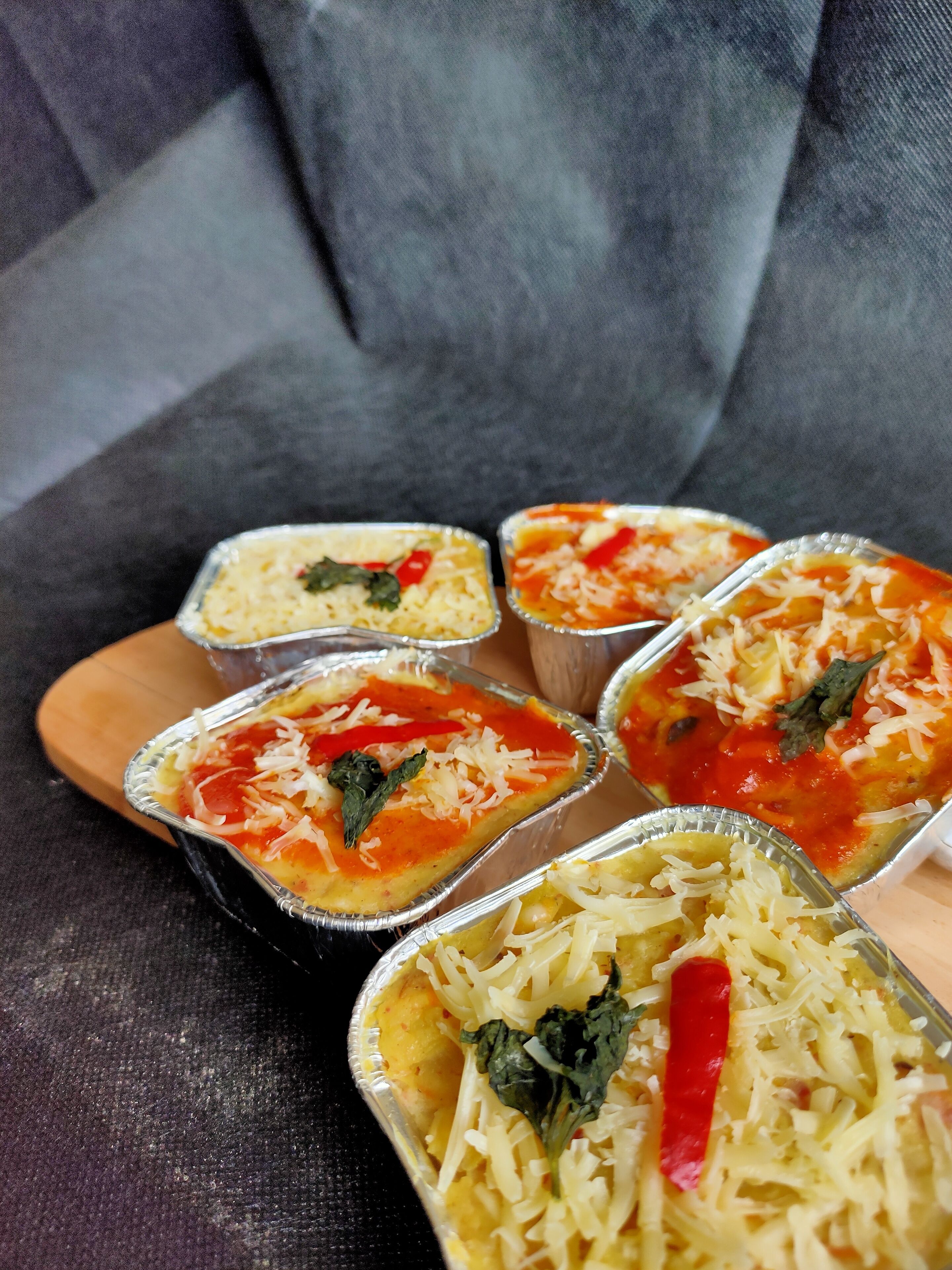 Eine Platte mit Essensbehältern und verschiedenen Gerichten, darunter eine Tomatensoße und geriebener Käse, auf einer Holzbrett.