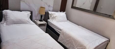 A hotel room with two beds, a marble wall, a mirror, and a nightstand with a lamp.