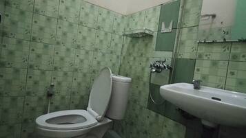 Un baño con inodoro y lavamanos, ambos con sanitarios blancos. Las paredes están cubiertas de azulejos con un estampado floral verde.