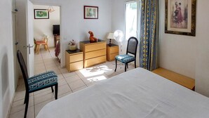 Un dormitori amb llit, cadira, prestatge, escriptori i televisió.