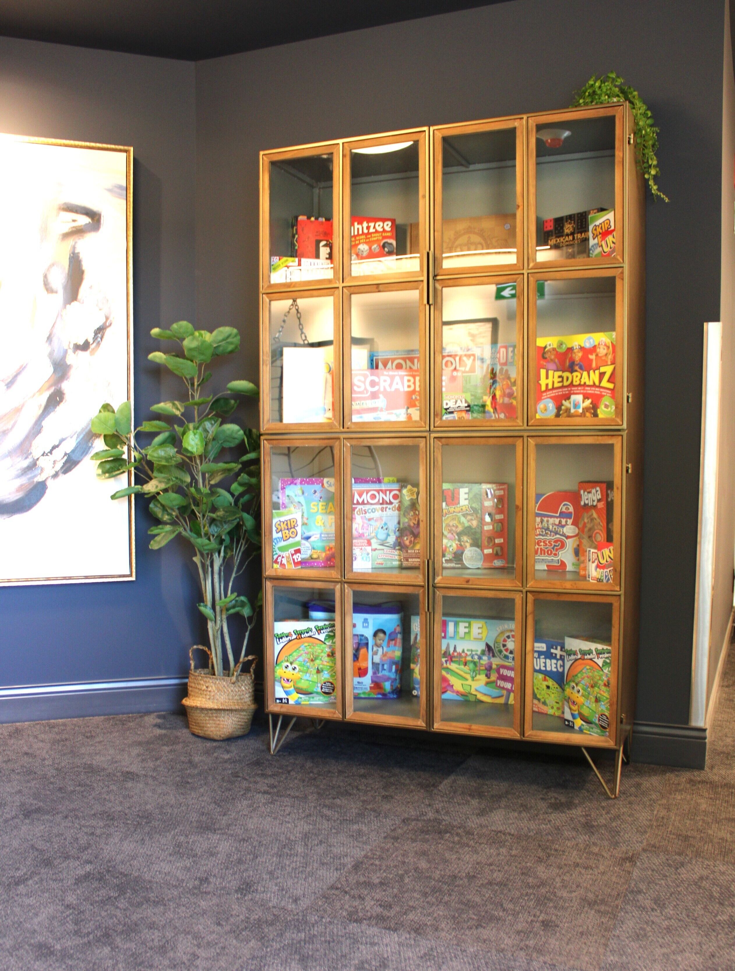 A wooden display cabinet with various board games and a potted plant.