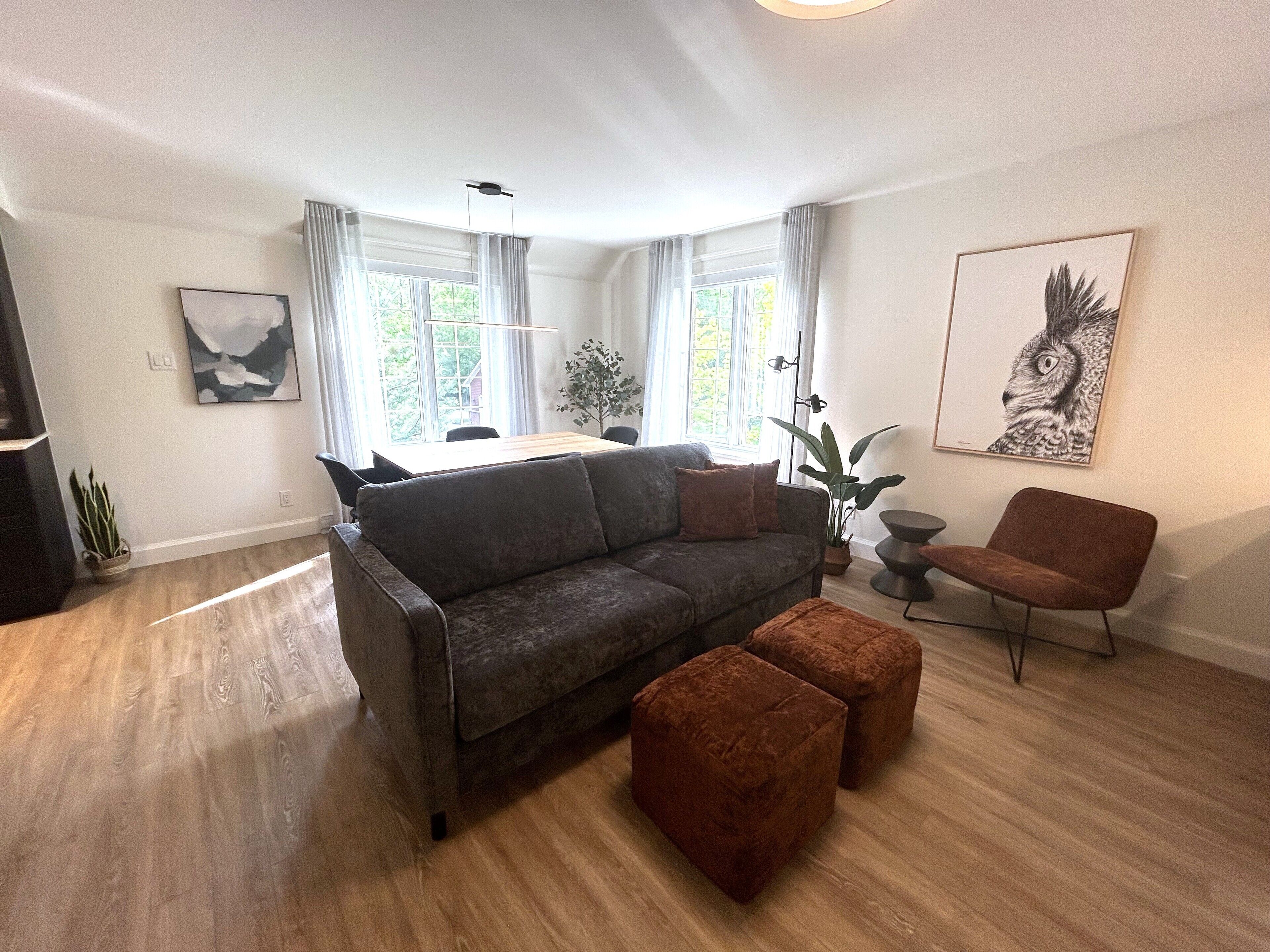 A modern living room with a grey sofa, two brown ottomans, a wooden dining table, and a dining chair.
