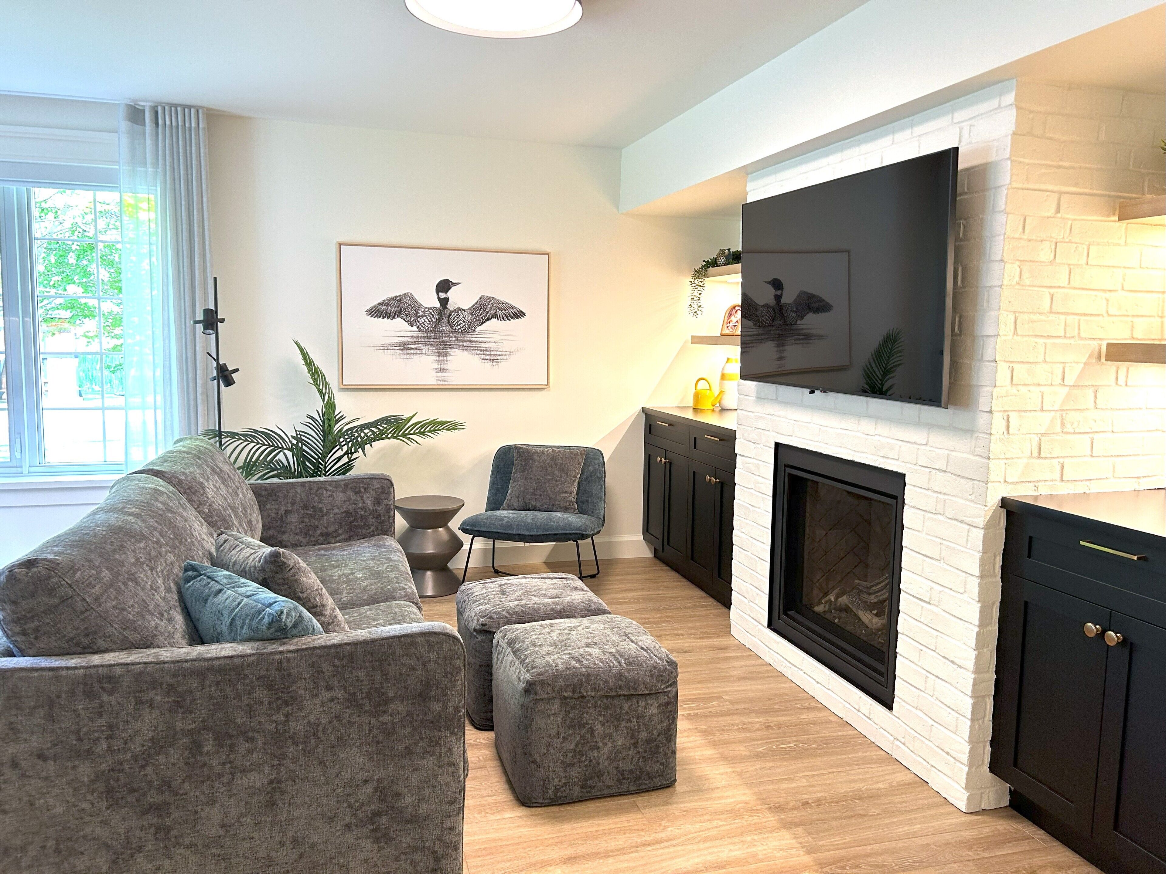 A modern living room with a sectional sofa, ottomans, a small side table, a fireplace, and a flat-screen TV mounted above it.