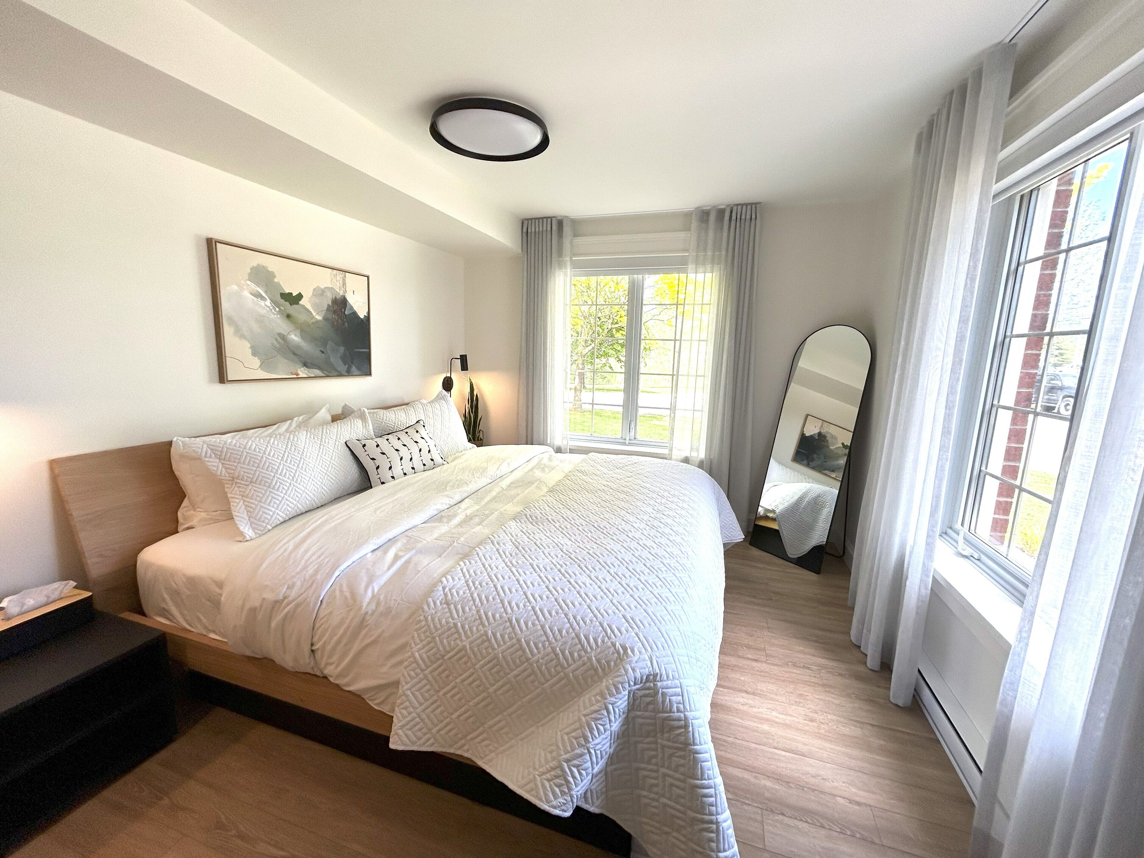 Een keurig opgemaakt slaapkamer met een bed, nachtkastje en een raam met gordijnen.