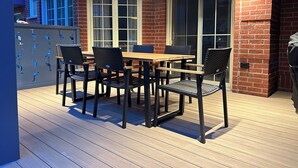 An outdoor patio with a wooden table and chairs, brick walls, and large windows. - Le Héron - Studios Nature (Magog)