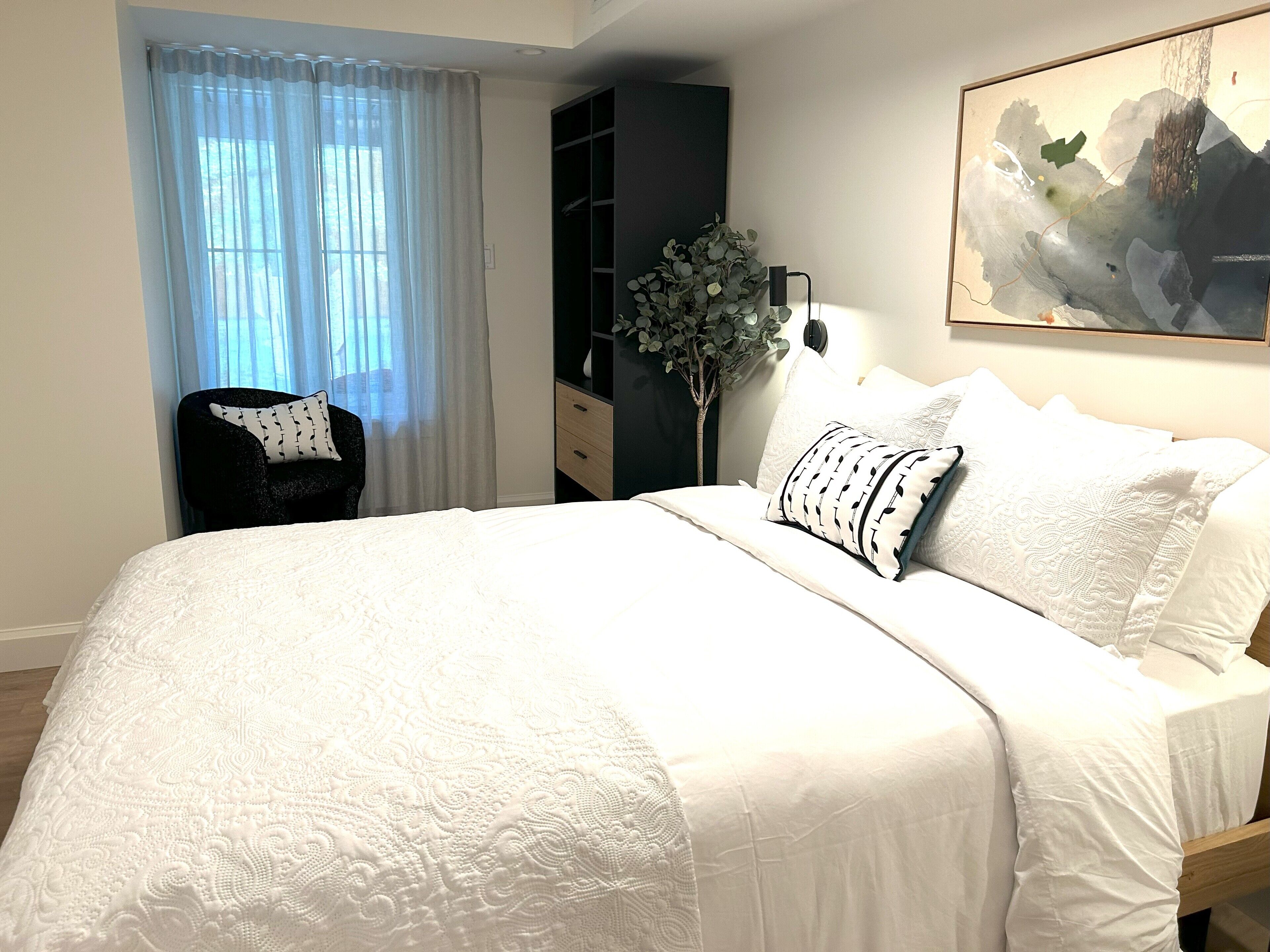 Une chambre à coucher bien rangée, avec un grand lit, une chaise, une armoire et un tableau accroché au mur.