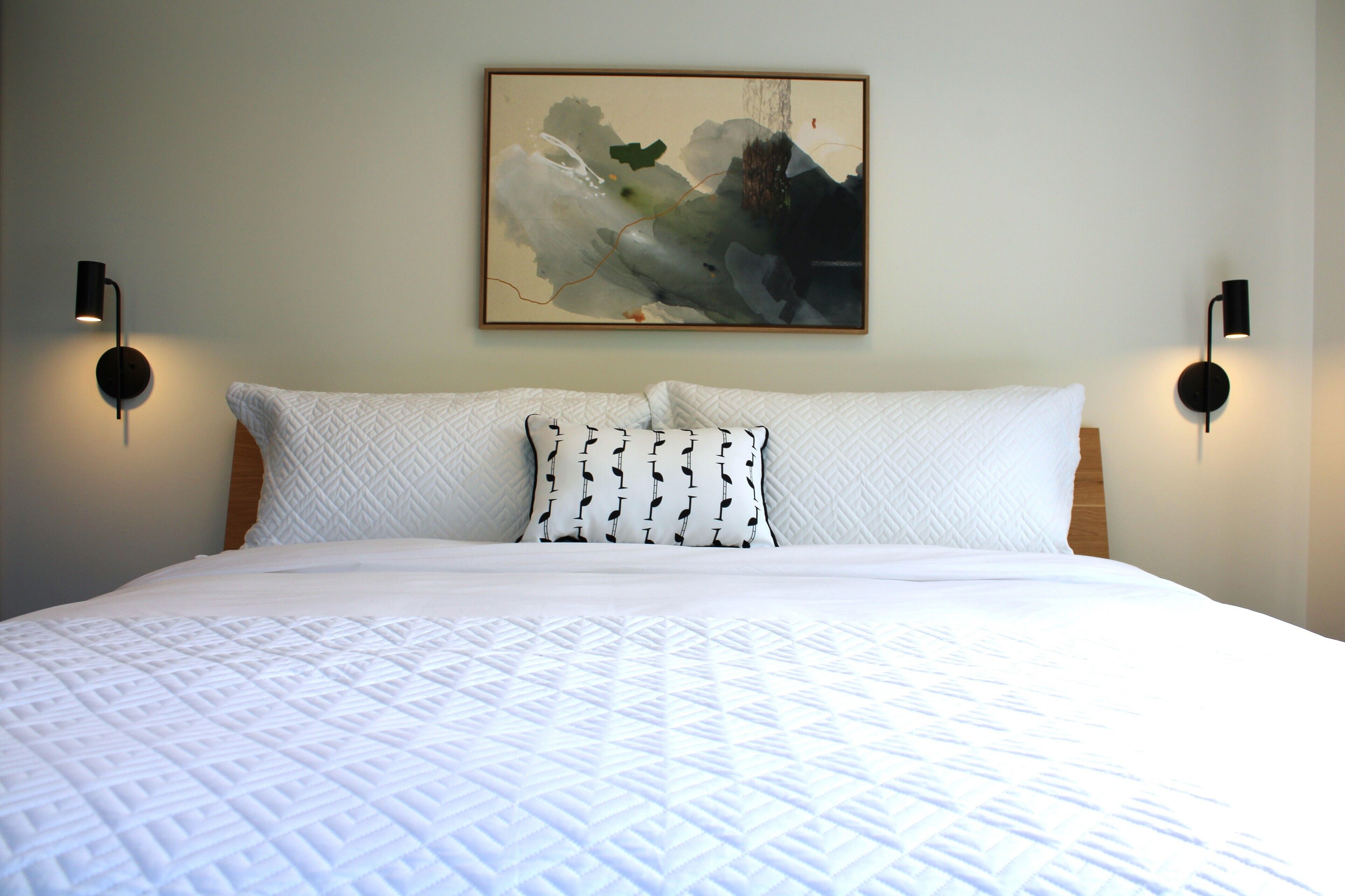A neatly made bed with a quilted white bedspread and two pillows, one plain and one with a black pattern.