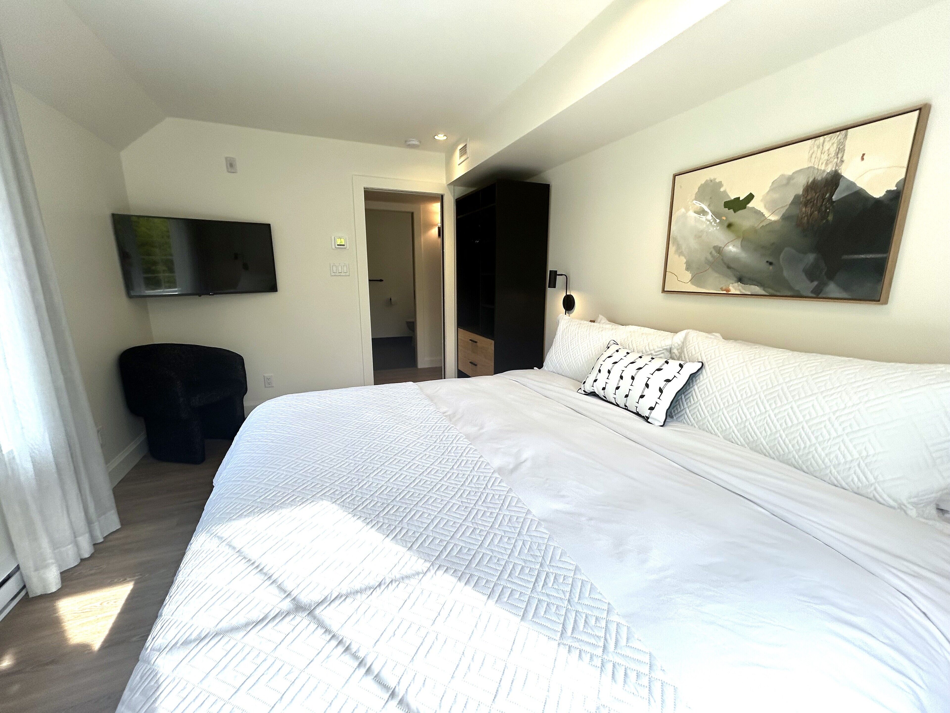 Une chambre d’hôtel avec un grand lit, un téléviseur à écran plat fixé au mur et un tableau au-dessus du lit.