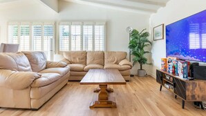 A living room with a beige sectional sofa, a wooden coffee table, and a TV on a wooden stand. - Family Vacation Home, Spa & Big Pool, Game Room, 8 minutes to Disney✨ (Anaheim)