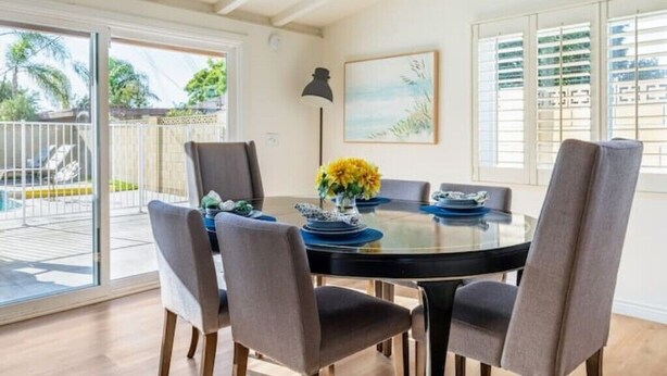 A dining area with a glass table, four chairs, and a vase of yellow flowers. - Family Vacation Home, Spa & Big Pool, Game Room, 8 minutes to Disney✨ (Anaheim)