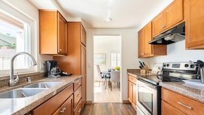 A modern kitchen with granite countertops, stainless steel appliances, wooden cabinets, and a view to a dining area. - Family Vacation Home, Spa & Big Pool, Game Room, 8 minutes to Disney✨ (Anaheim)