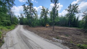 Un chemin de terre avec un engin de chantier jaune dans une zone boisée.