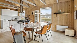 Une cuisine moderne avec des meubles blancs, un coin repas doté d’une table ronde et de chaises en cuir, et une grande fenêtre offrant une vue sur l’extérieur.