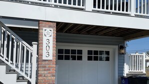 Ein zweistöckiges Haus mit überdachter Garage, einer Ziegelssäule mit der Nummer 303 und einer Treppe, die zum oberen Stockwerk führt.