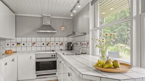 Una cocina moderna con armarios blancos, horno integrado y un amplio ventanal con vistas a zonas verdes.