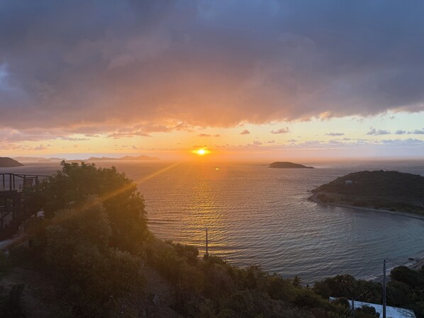 Un coucher de soleil sur une étendue d’eau, avec des reliefs lointains et une petite construction sur une île.
