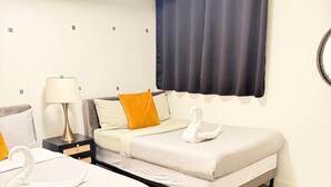 Quarto de hotel com duas camas, uma mesa de cabeceira com abajur, uma janela com cortinas e um espelho fixado na parede.