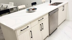 Cozinha moderna com bancada branca, pia de aço inoxidável e armários de madeira clara.