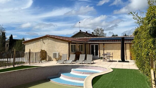 A residential property with a swimming pool, a patio with lounge chairs, and a house with a tiled roof.