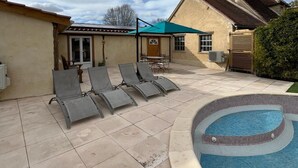 A backyard with a swimming pool, lounge chairs, and a covered patio area.