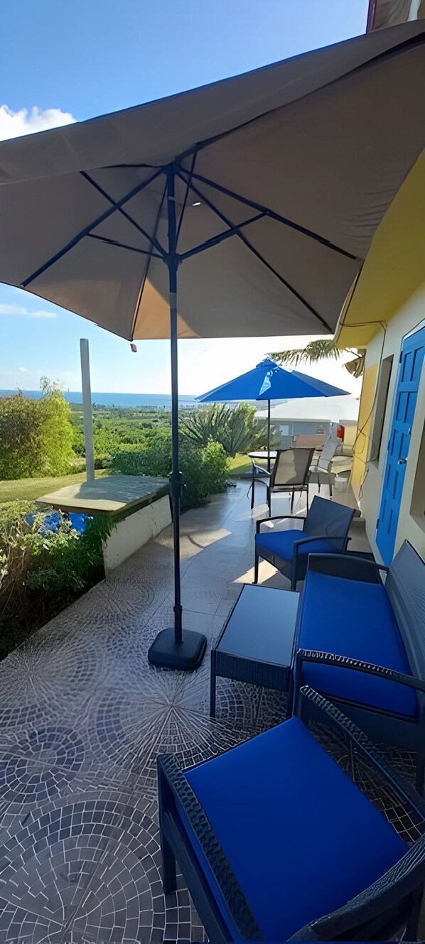 An outdoor patio with a table and chairs, a large umbrella, and a view of the landscape.