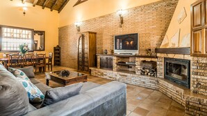 A cozy living room with a brick fireplace, a television, and a dining area with wooden furniture. - Cozy home in Salar with indoor swimming pool (Salar)