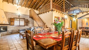 A spacious dining area with a wooden table set for a meal, a fireplace, and a staircase leading to an upper level. - Cozy home in Salar with indoor swimming pool (Salar)