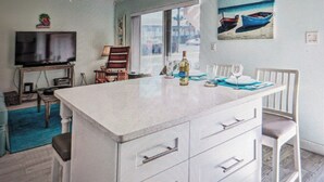Une cuisine moderne dotée d’un grand îlot central, d’un coin repas avec une table et des chaises, d’un téléviseur et d’un ventilateur de plafond.