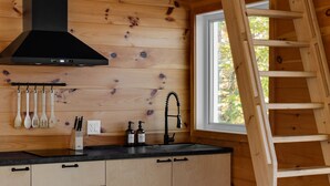 A wooden cabin kitchen with a black range hood, wooden utensils, a sink, and a wooden ladder. - Cozy cabin - lake view  (Lac-des-Îles)