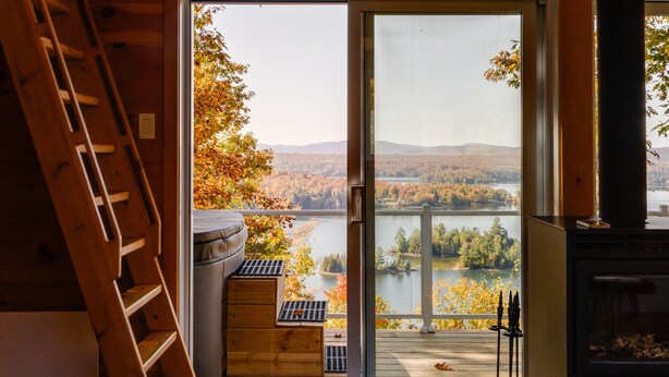 A wooden interior with a large window overlooking a scenic landscape. - Cozy cabin - lake view  (Lac-des-Îles)