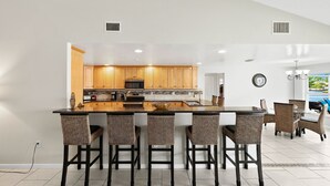Una cocina moderna con armarios de madera, una isla central con taburetes y una zona de comedor con sillas de mimbre.