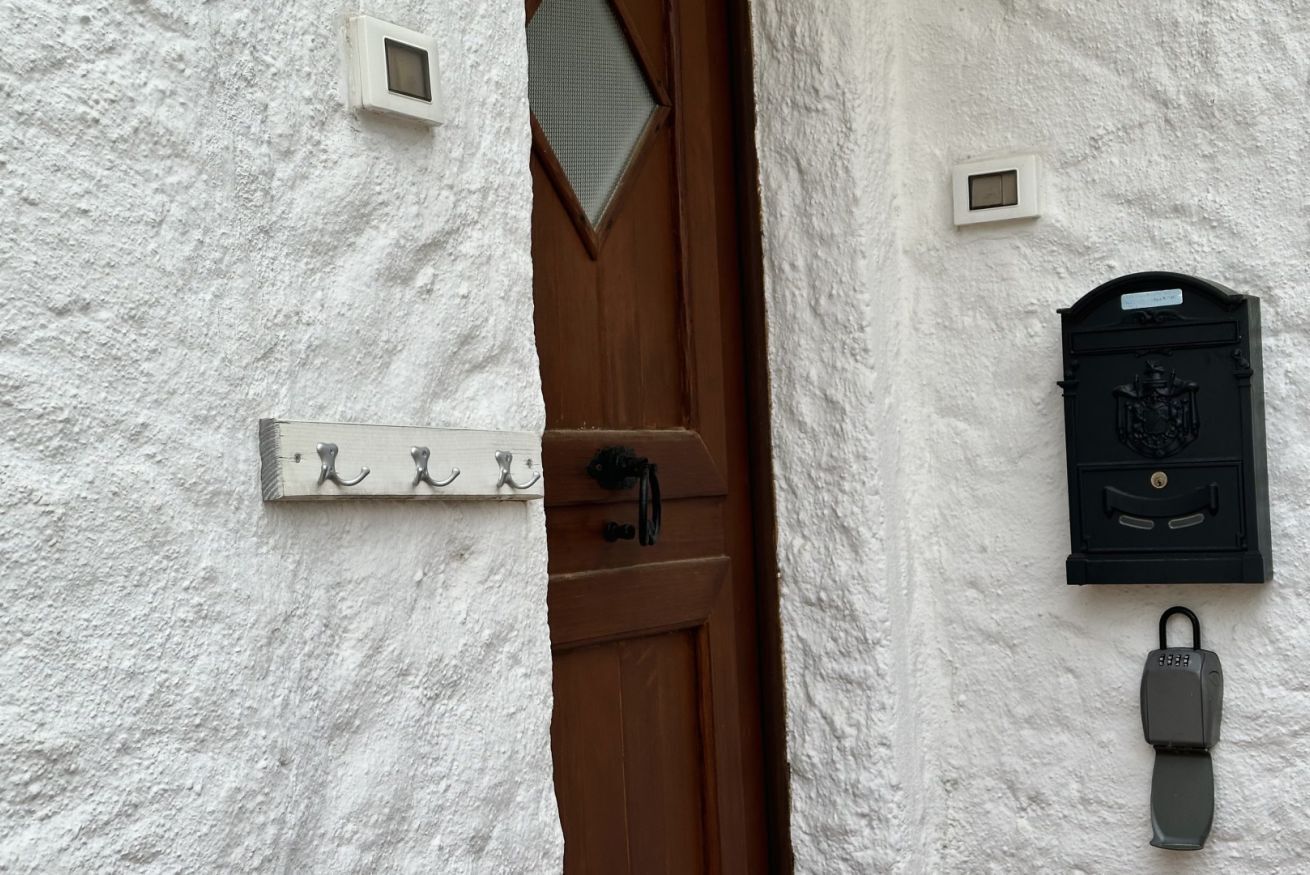 Un mur blanc à la texture particulière, avec une porte marron, une fente métallique pour le courrier et une serrure à clé.