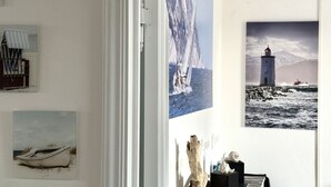 Ein Zimmer mit weißer Wand, einer Tür und drei gerahmten Bildern, die maritime Szenen zeigen.