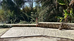 Una zona pavimentada amb lloses de pedra, envoltada de vegetació i un mur de pedra.