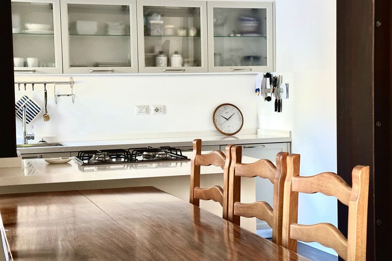 Eine moderne Küche mit weißen Schränken, einem Gasherd, einem Holztisch und einer Uhr an der Wand.