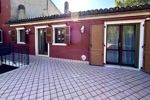 Een gebouw met een betegeld terras, houten luiken en een pannendak.