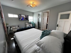 Ein Hotelzimmer mit einem großen Bett, einem an der Wand montierten Fernseher, einem Schreibtisch mit Stuhl und einem begehbaren Kleiderschrank.